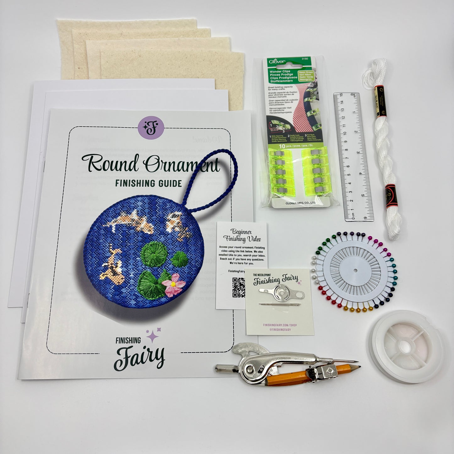 Beginner Finishing Kit contents laid out including matboard, batting, wonderclips, cording, lacing thread, and project bag for finishing needlepoint round ornaments