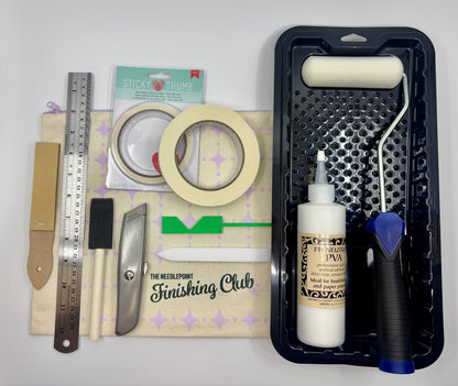 Cartonnage Essential Supplies kit for needlepoint finishing, including utility knife, teflon folder, corner cutter, acid-free tapes, PVA glue, foam brush, roller, metal ruler, and project bag

