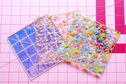 Feral Notions 5 inch square rulers shown in all three colorways, Golden, Confetti, and Iridescent, curated by the Needlepoint Finishing Fairy for needlepoint finishing
